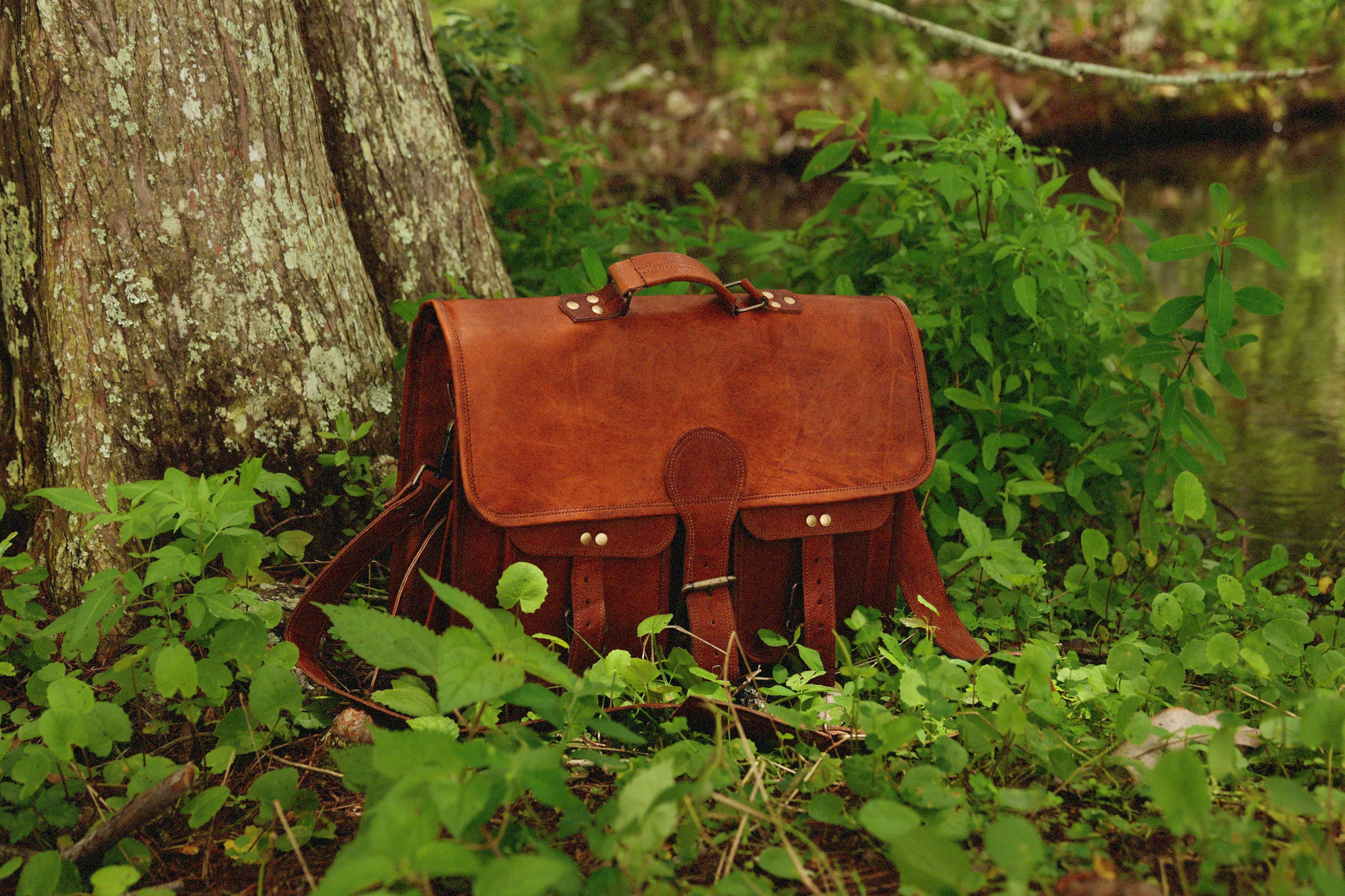 Leather satchel shown next to a pond in a wooded area