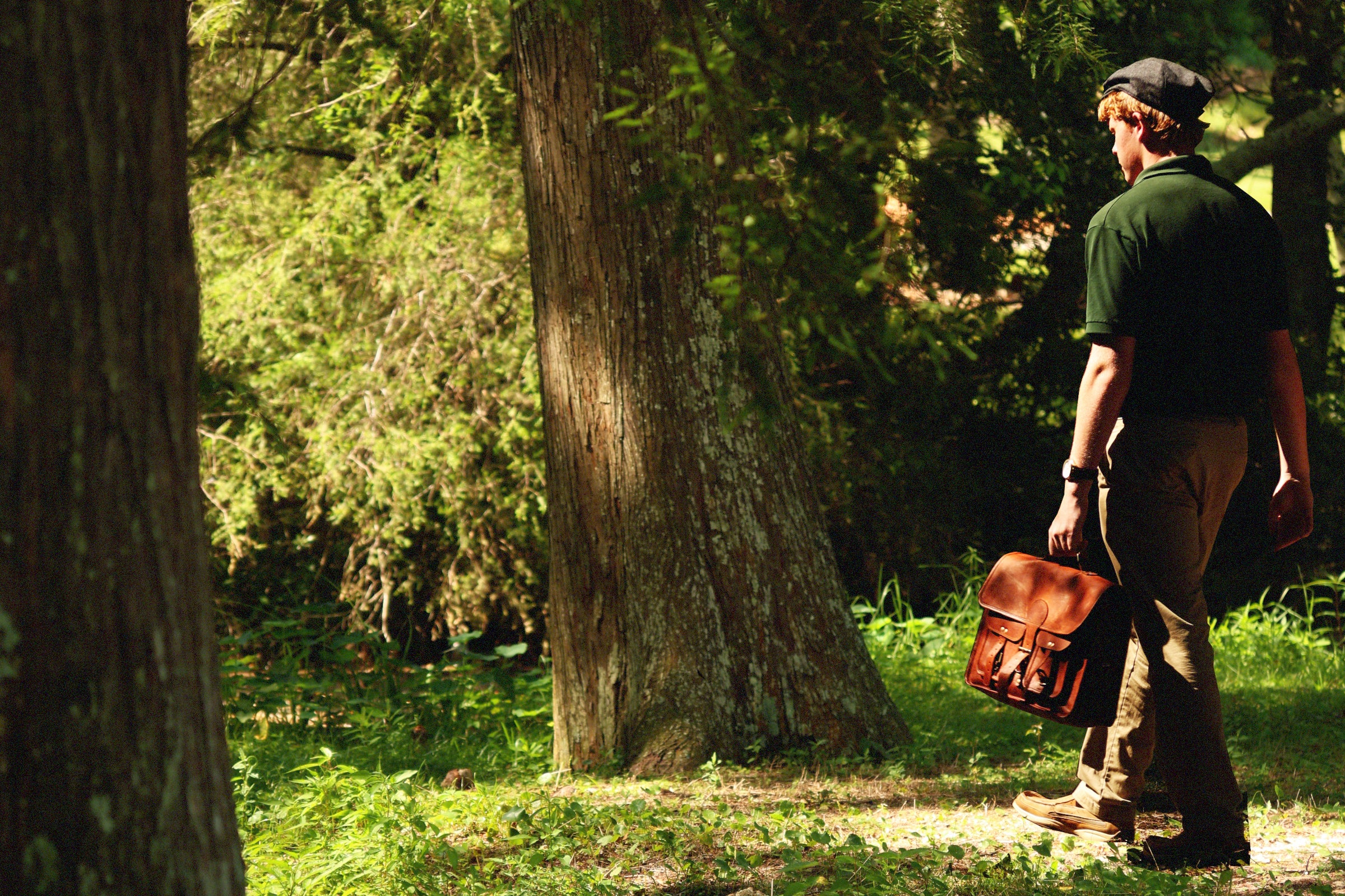 Model walking through a forest with a leather satchel